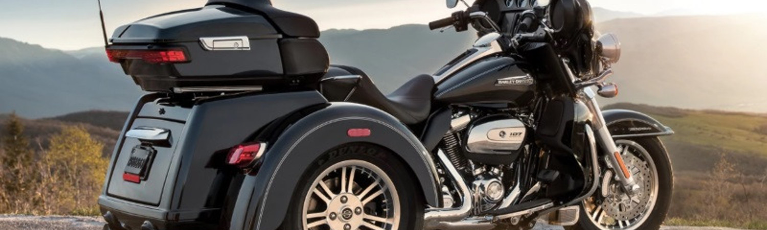 A Harley-Davidson® FLHTCUTG Tri-Glide® Ultra motorcycle parked on a road overlooking foggy hills.