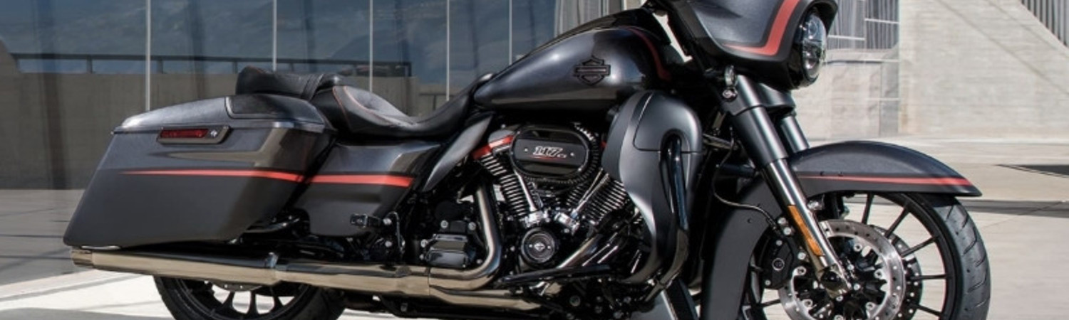 A red and black Harley-Davidson® FLHXSE CVO™ Street Glide® parked mid-day in-front of an urban building.